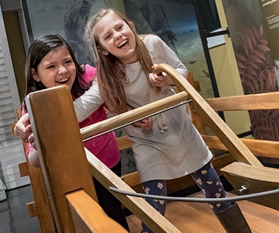 Two young girls testing their strength with the original John Deere plow interactive