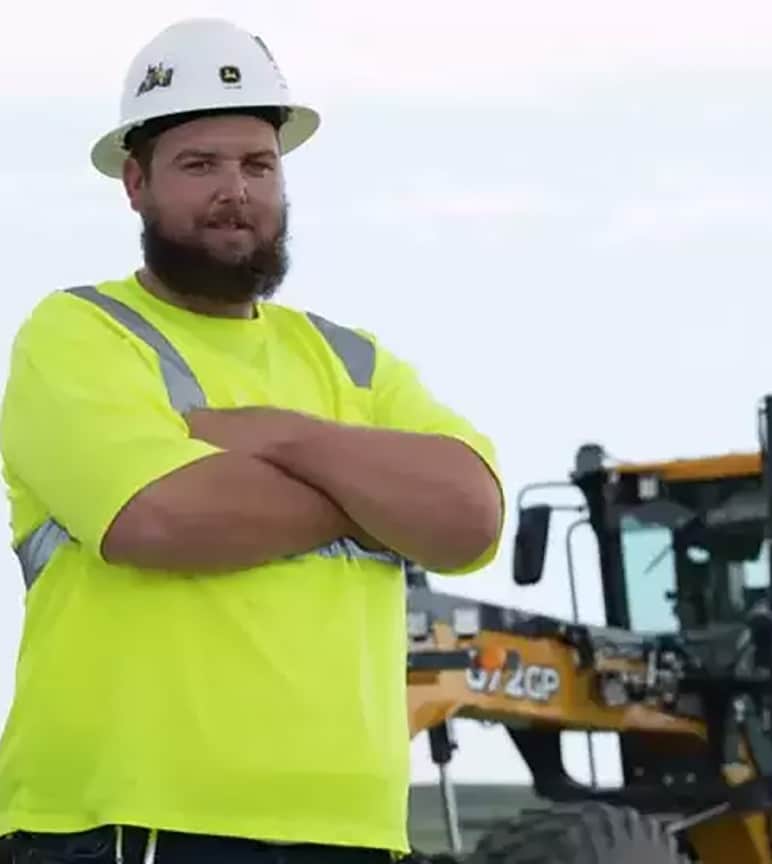 Ryan standing in front of Deere construction equipment with folded arms